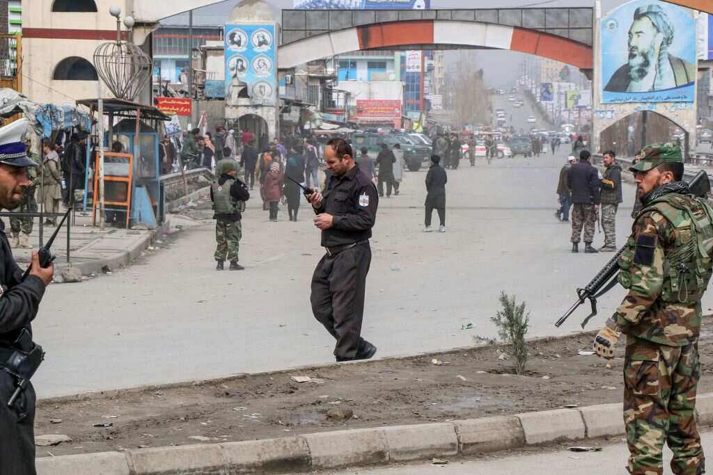 Afghan security forces personnel stand guard on a road near the site of a gun attack