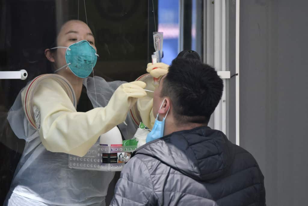 A medical staff member in a booth takes samples from a visitor for coronavirus test at a walk-thru testing station set up at Jamsil Sports Complex in Seoul