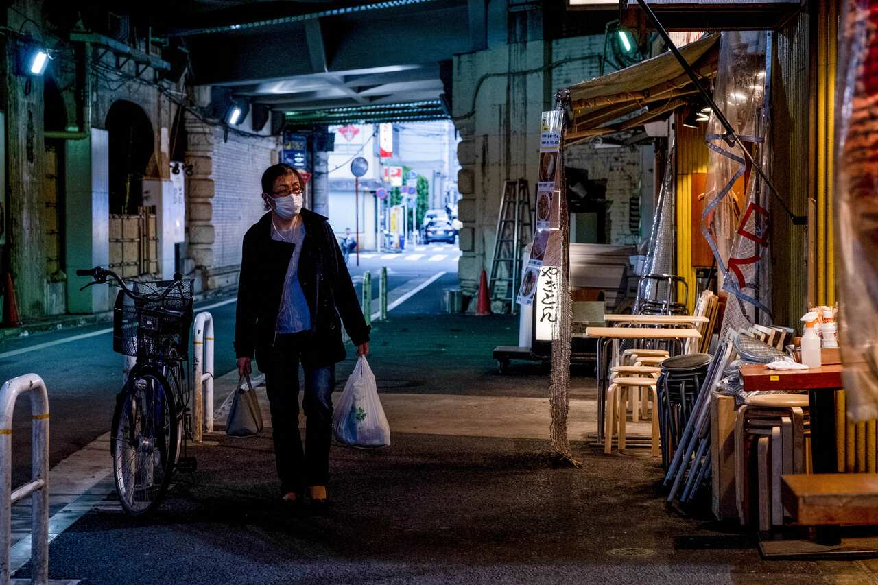 A woman walks along an empty Tokyo street while wearing a face mask.