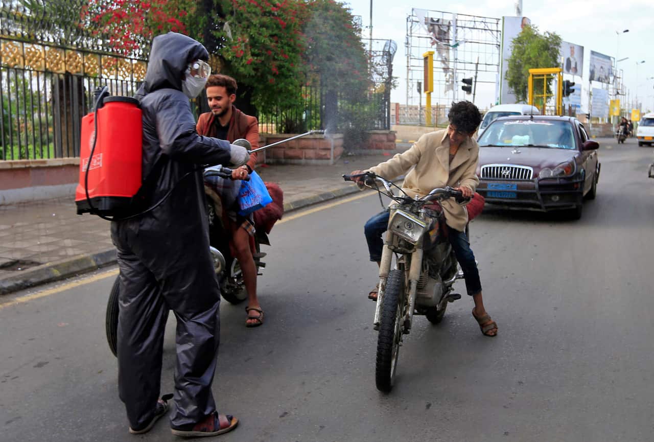 Yemeni security personnel disinfect a man on a motorcycle.