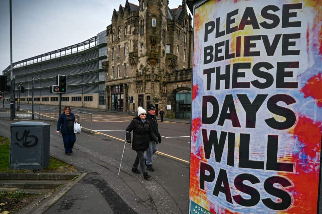 Members of the public walk past new posters placed around the city center in Glasgow, Scotland. 