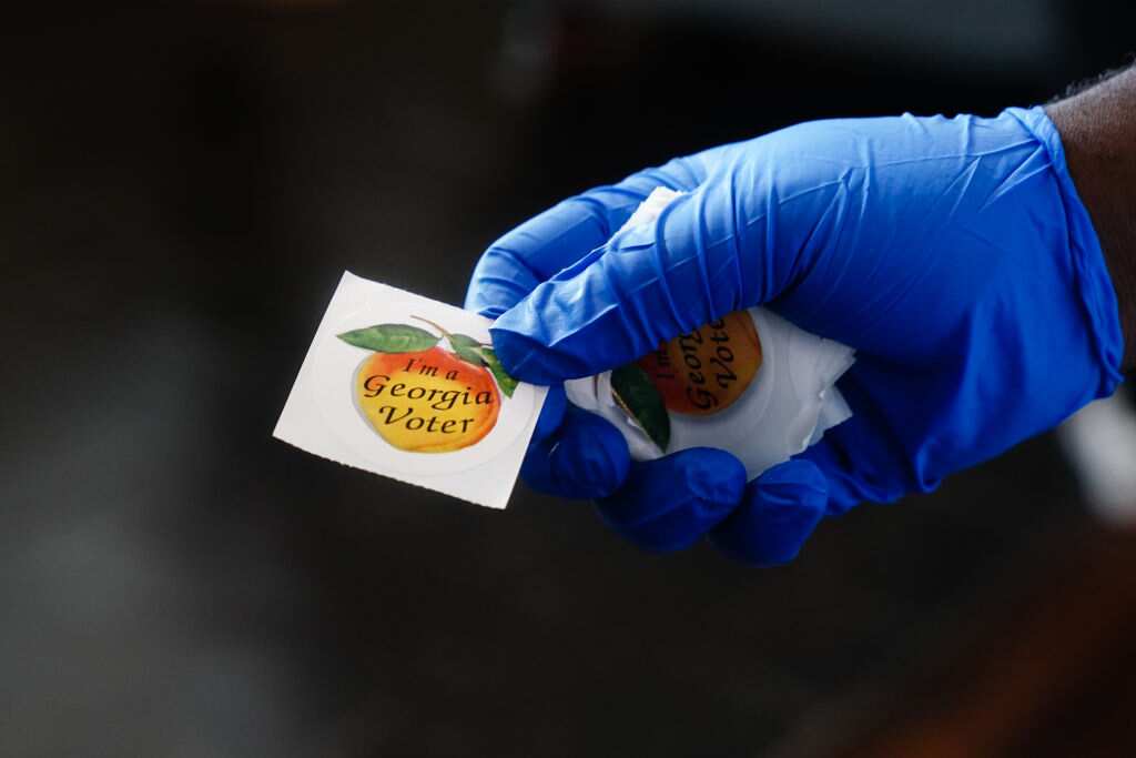 A polling place worker holds an "I'm a Georgia Voter" sticker to hand to a voter in June 2020 in Atlanta, Georgia.