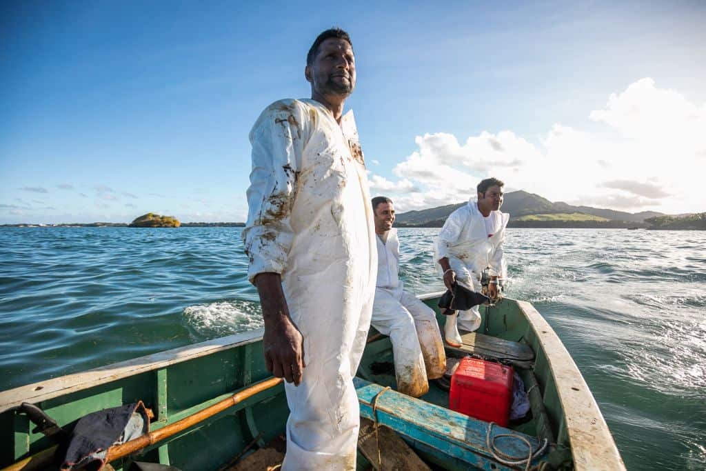 Fishermen look on while they place handmade oil barriers into the sea