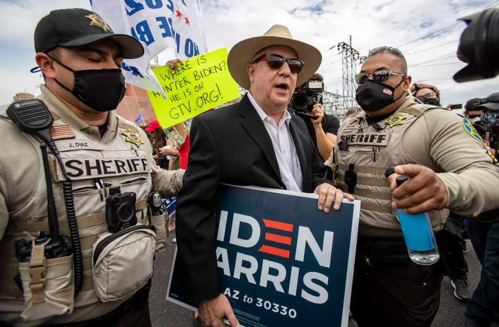 Police officers escort Biden supporter Ron Russ away from pro-Trump protesters who have gathered in the parking lot of the Maricopa County Elections Building.