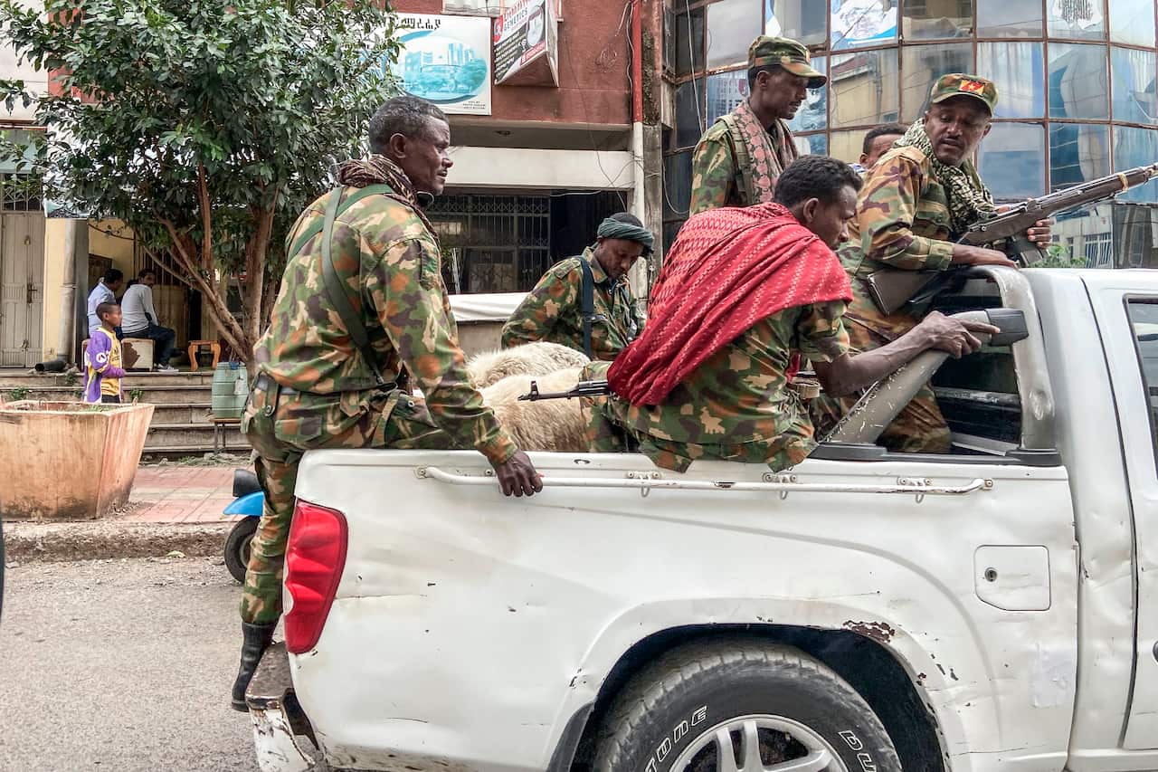 Men with army uniforms and guns ride on the back of a utility vehicle