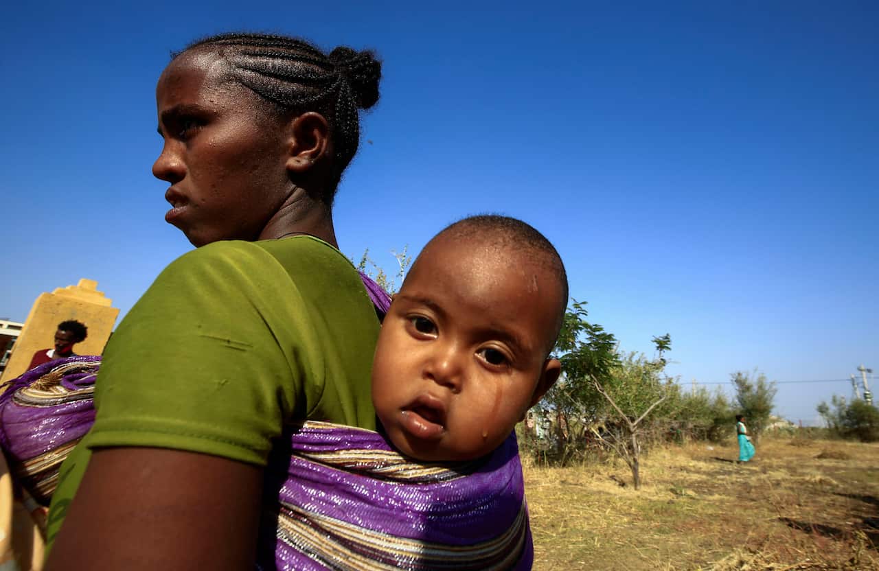 An Ethiopian refugee who fled fighting in the Tigray Region carries her baby on her back at the Village 8 border reception center in Sudan's eastern Gedaref State.