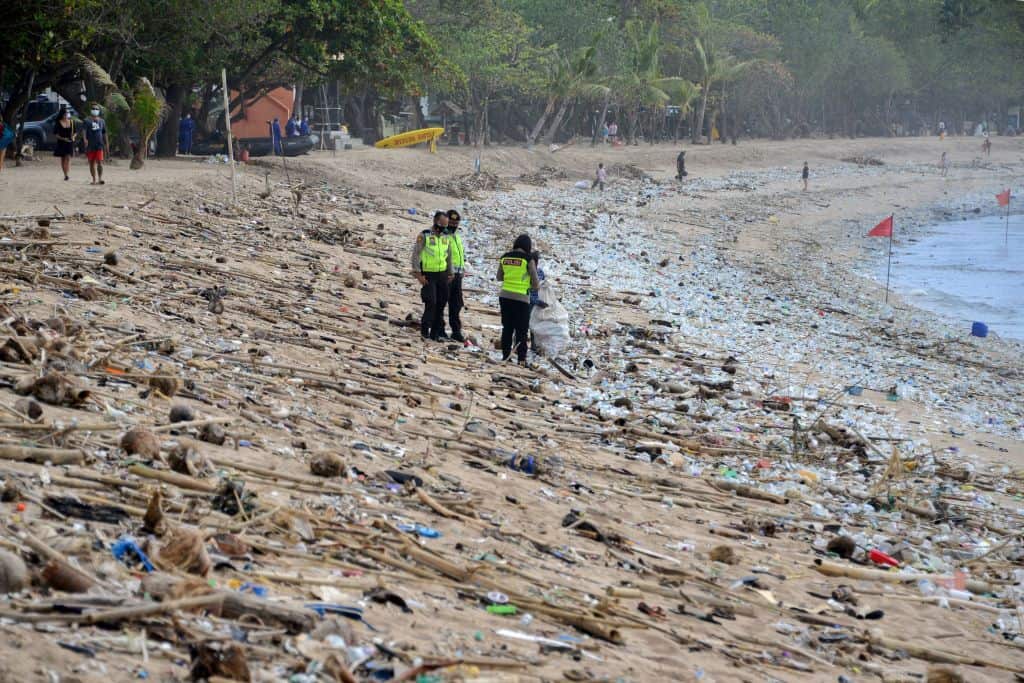 Police stand amongst rubbish washed up on Kuta Beach, Bali.