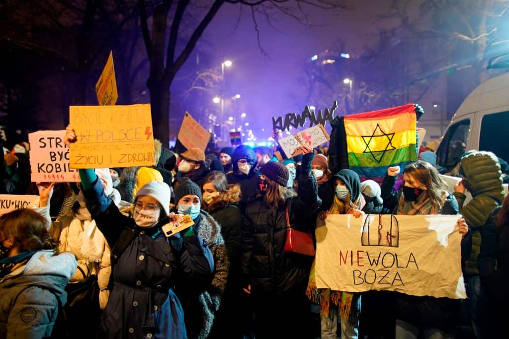 People hold signs reading (L) 'Being a woman in Poland endangers your life and health' and (R) 'Bondage to god' as they take protest in Warsaw on 28 January.