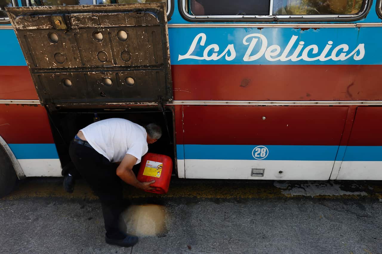 A bus driver tops up some fuel with a canister to make it to a petrol station, where trucks often queue for hours due to fuel shortages in Venezuela.