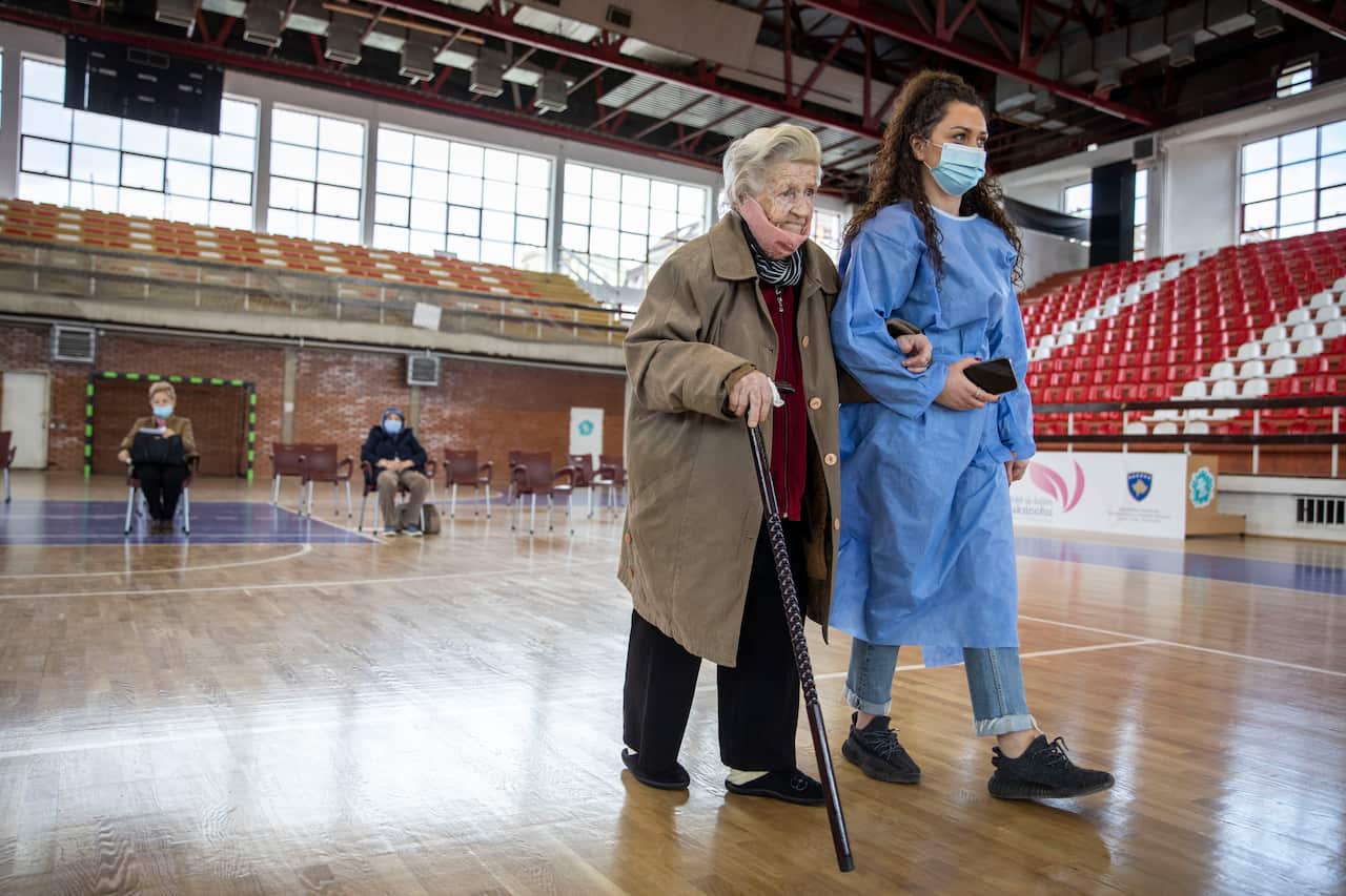 An elderly woman is being accompanied before receiving a dose of the AstraZeneca vaccine from Kosovo’s first COVAX supply as the nation begins its rollout for people aged over 85 on 8 April.
