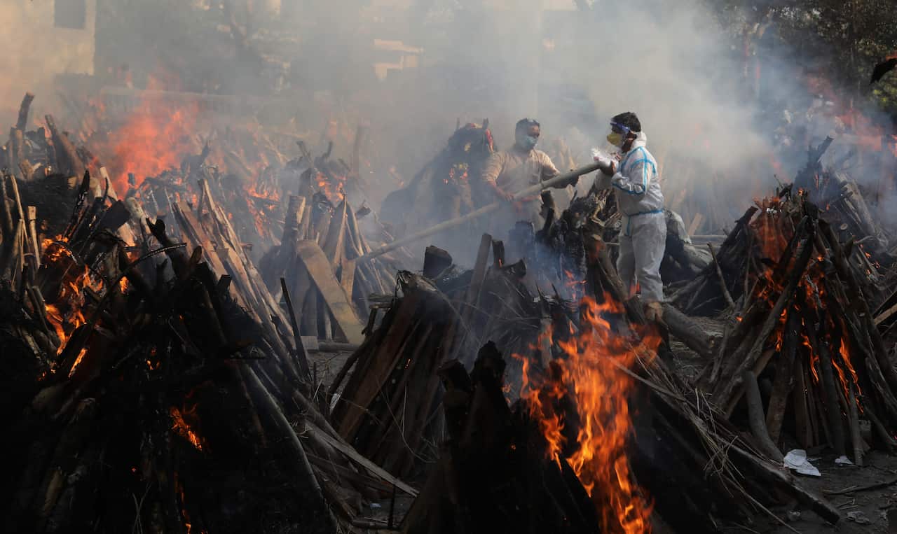 Relatives stand next to the burning funeral pyres of those who died due to the coronavirus disease.