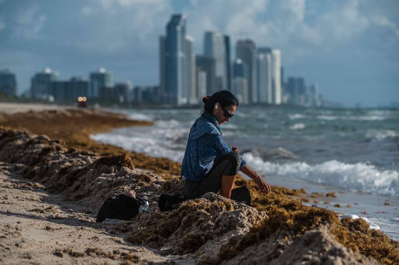 A neighbour sits on the waterfront as she pays her respects near the partially collapsed Champlain Towers South building on 28 June 2021, in Florida.