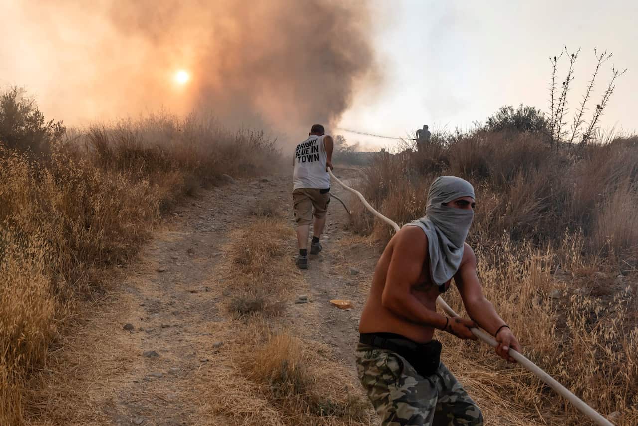 Volunteers help carry a firehose in an effort to contain a fire near the Kotsiatis area, on the outskirts of Cyprus' capital Nicosia on 4 July, 2021.