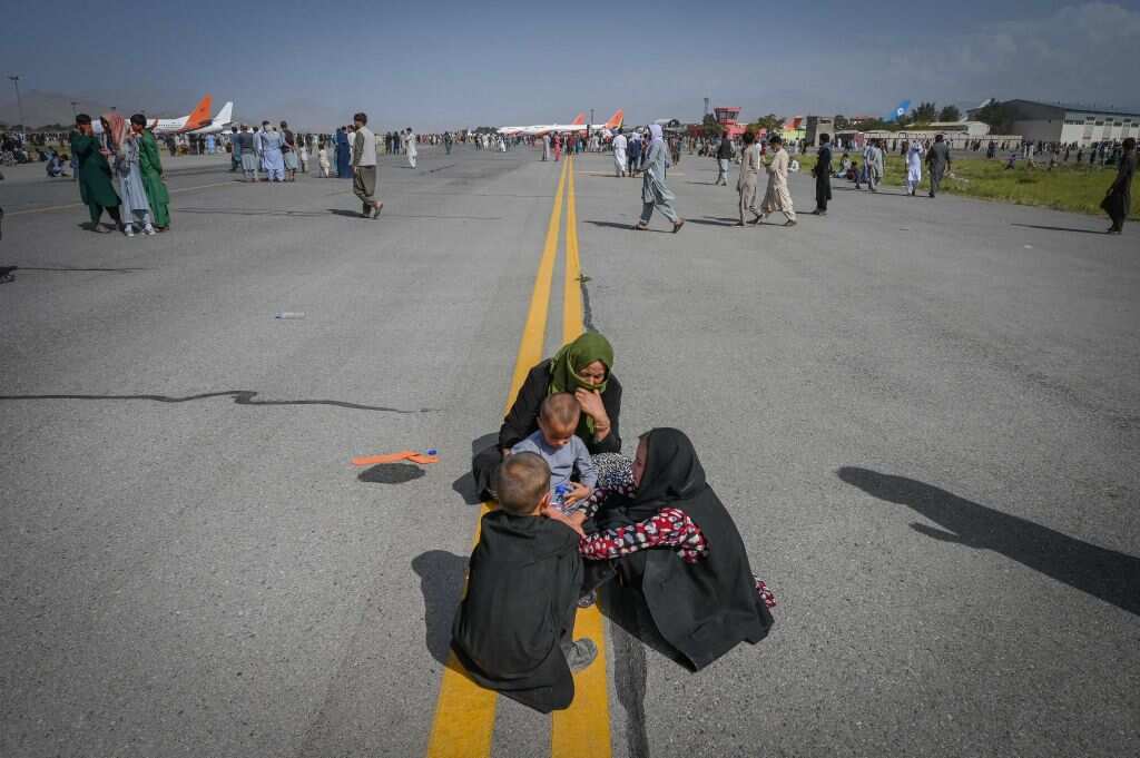 Afghan people sit as they wait to leave the Kabul airport in Kabul on 16 August, 2021. 