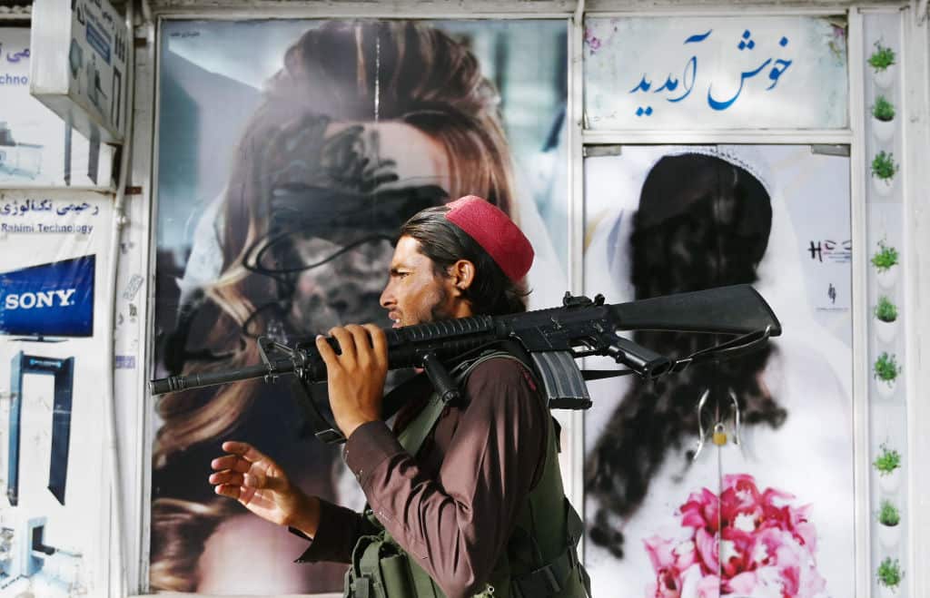 A Taliban fighter walks past a beauty salon with images of women defaced using spray paint in Kabul on August 18, 2021.