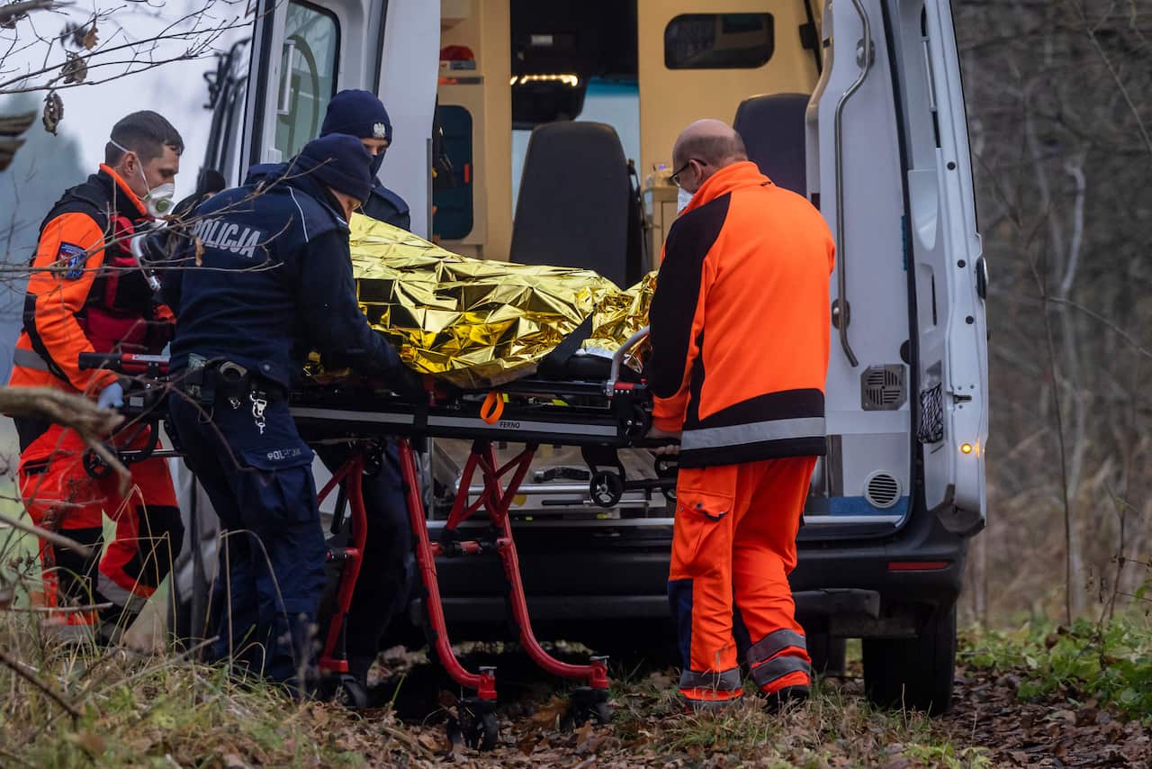 Paramedics take an injured refugee to an ambulance as police and border guards officers detain refugees near Hajnowka, Poland.
