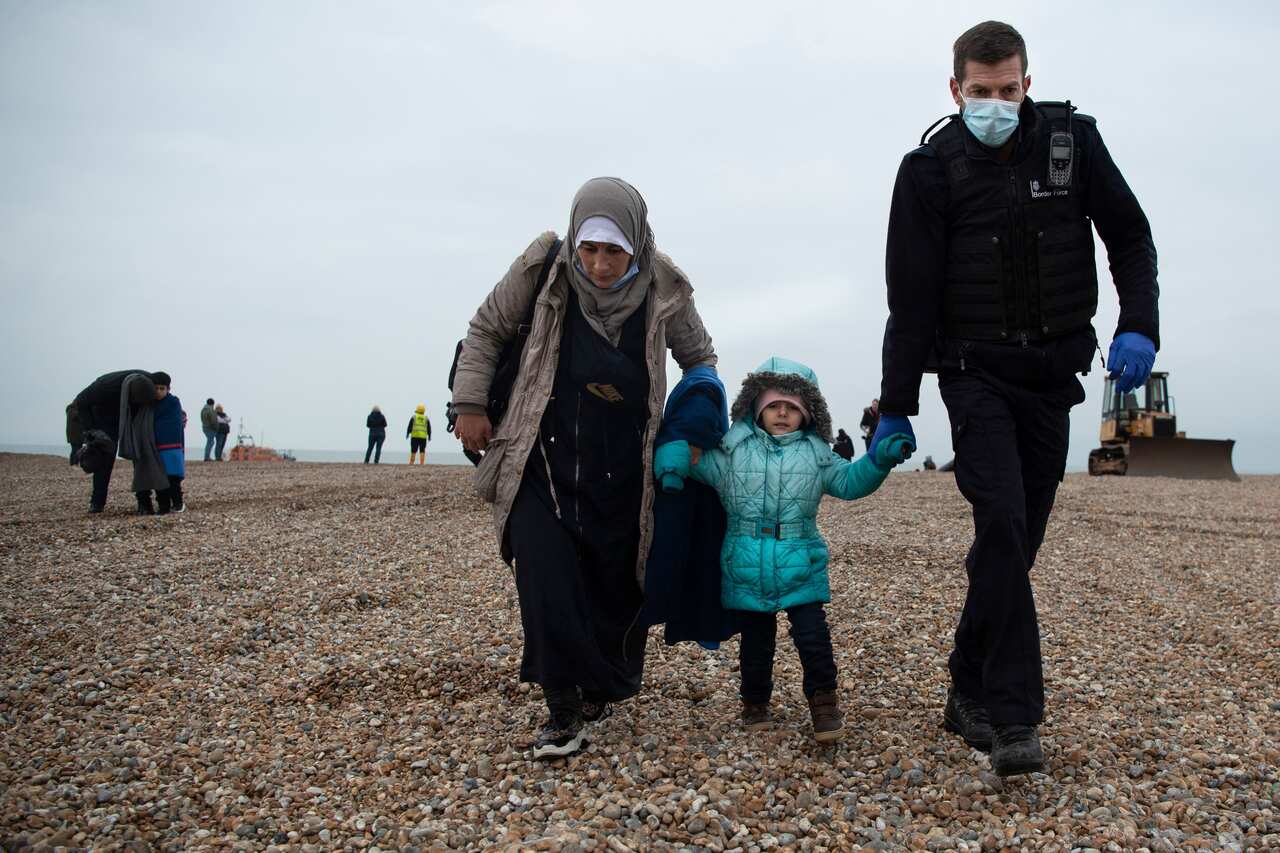 A member of the UK Border Force () helps migrants on a beach in Dungeness on November 24, 2021, after they were rescued while crossing the English Channel. 
