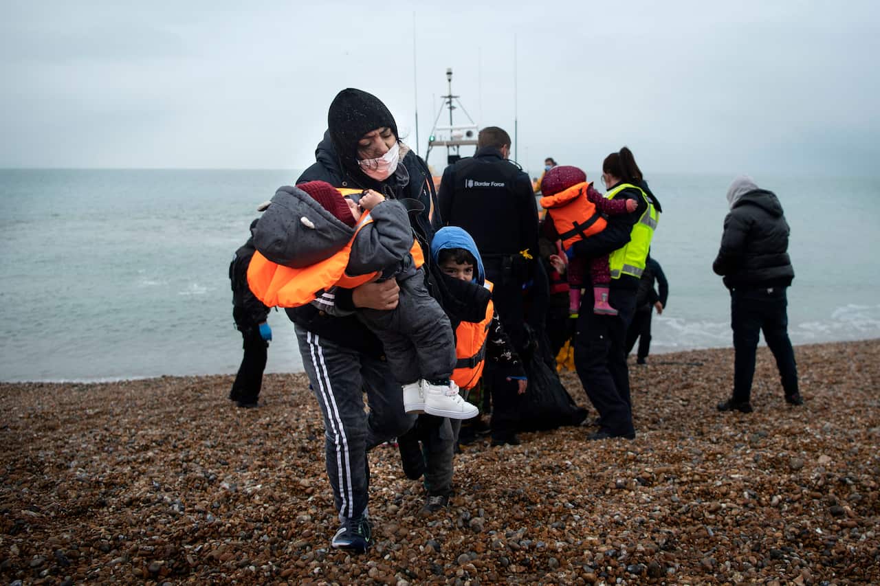 A migrant carries her children after being helped ashore from a RNLI (Royal National Lifeboat Institution) lifeboat at a beach in Dungeness, on the south-east coast of England, on November 24, 2021, after being rescued while crossing the English Channel. 