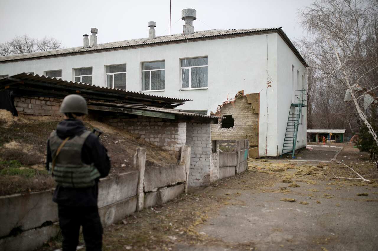 A Ukrainian soldier stands next to a damaged wall after the reported shelling of a kindergarten in the settlement of Stanytsia Luhanska.