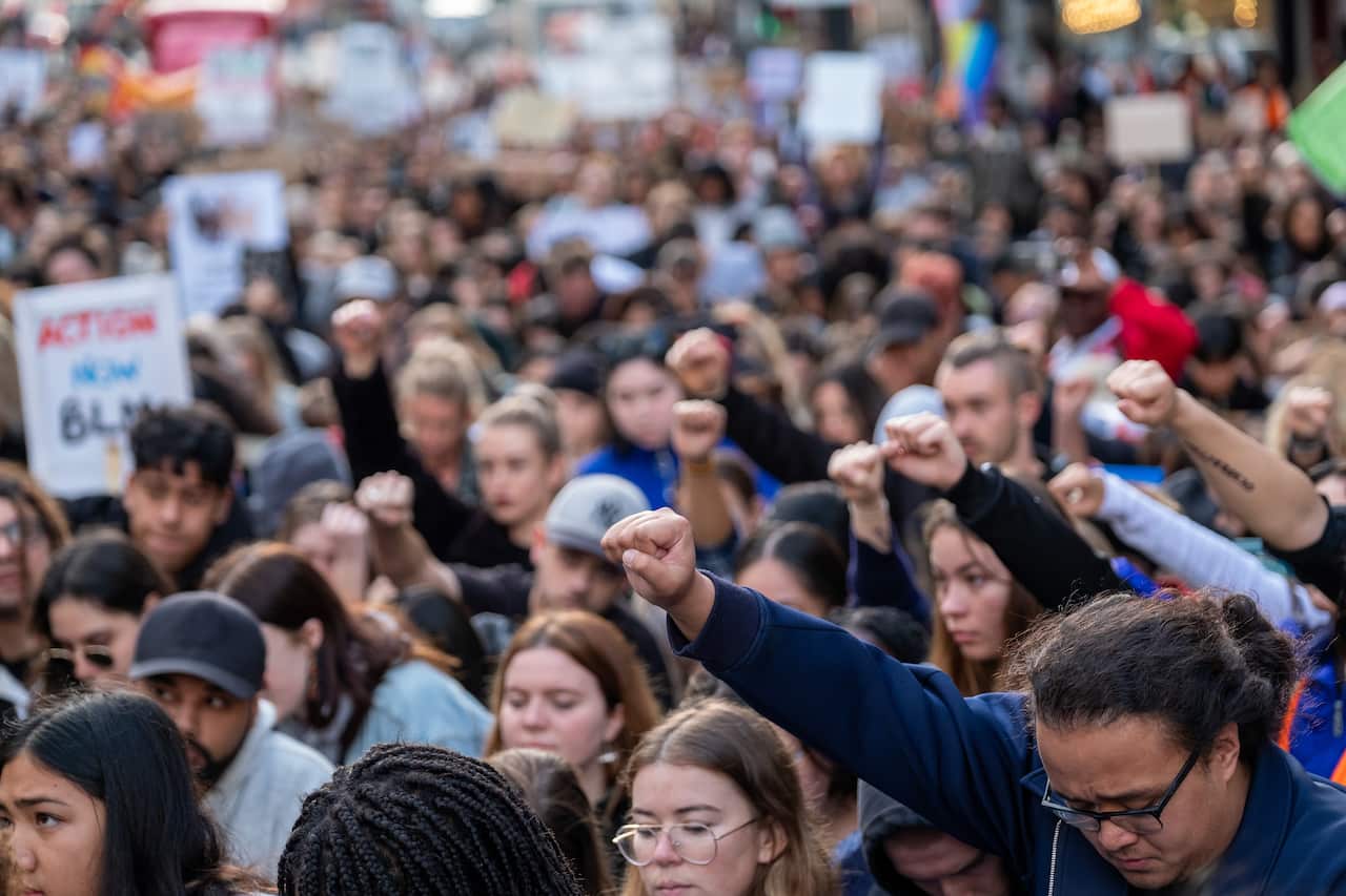 Protesters in Auckland take a knee and raise a fist during an organised march.