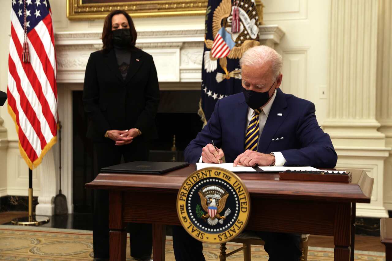 US President Joe Biden signs an executive order as Vice President Kamala Harris looks on at the White House 22 January, 2021.