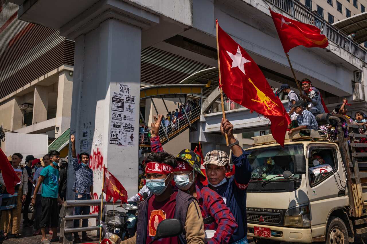 Protesters waving red NLD flags ride on trucks on 13 February, 2021 in Yangon, Myanmar.
