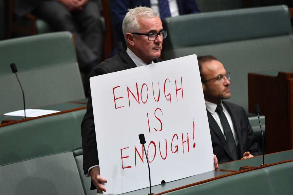 Member for Denison Andrew Wilkie holds up a sign reading "Enough is enough!" during Question Time in the House of Representatives on 15 March, 2021
