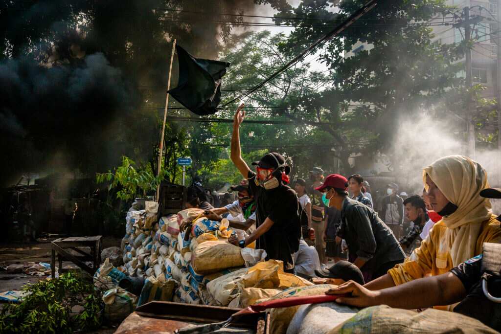 Anti-coup protesters shout slogans towards approaching security forces as smoke rises from burning car tires in Yangon, Myanmar on 28 March 2021.