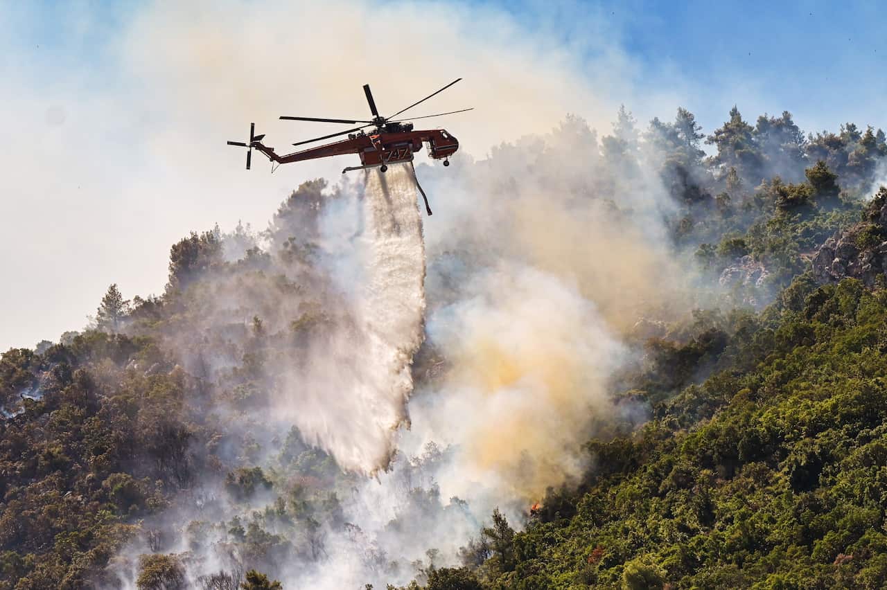 A helicopter drops water over fire in the Thrakomacedones area, in northern Athens, on 7 August, 2021