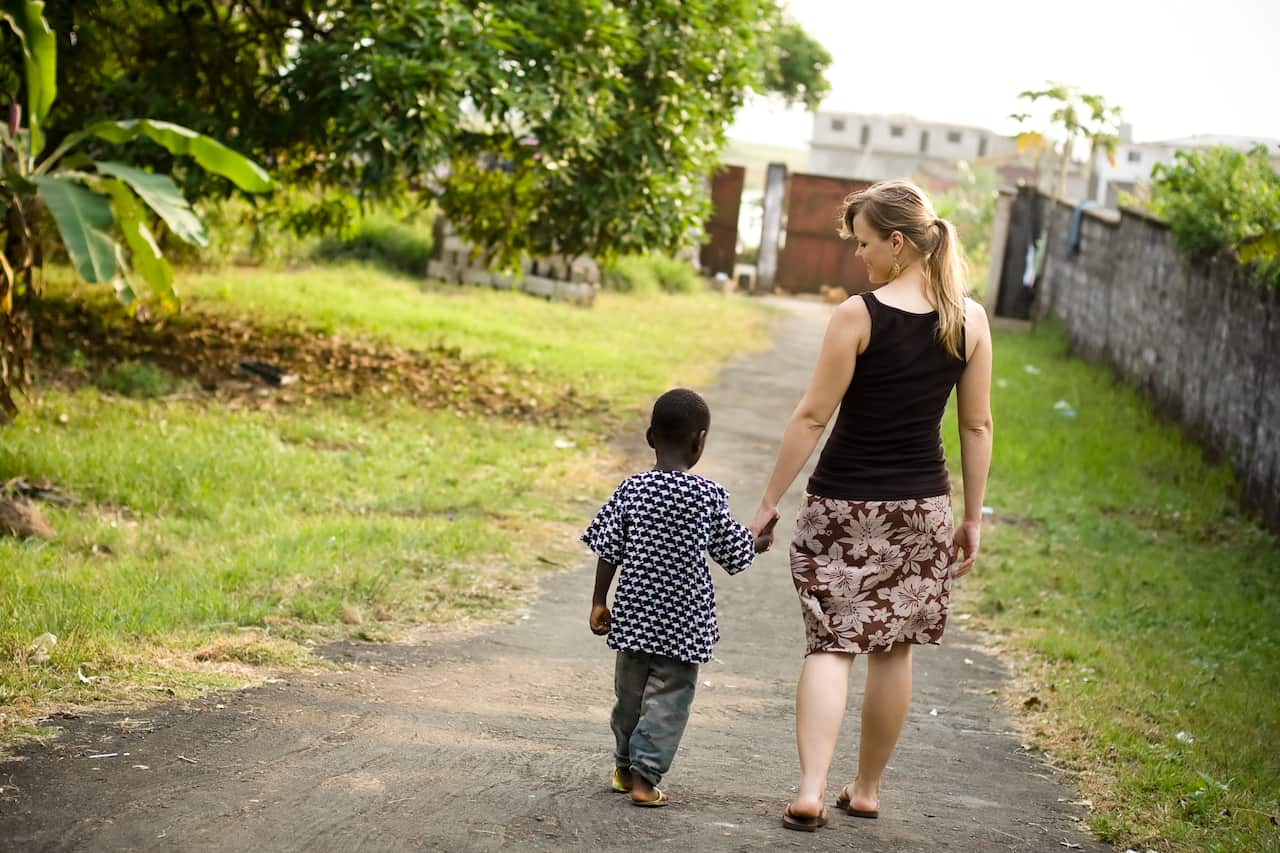 A Western woman walks hand in hand with an African child.
