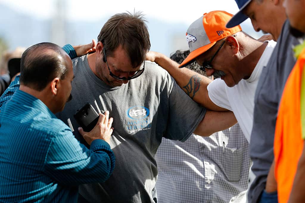 A group of men embrace in prayer outside the crime scene where the suspects in the shooting at the Inland Resource Center