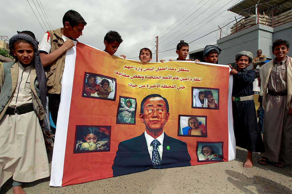 Yemeni children hold a banner depicting United Nations Secretary General Ban Ki-Moon with blood coming out of his eyes and dollar signs on his face.