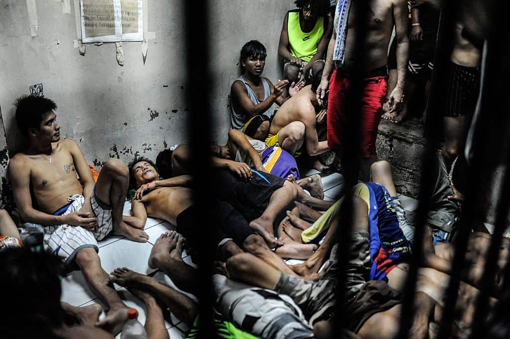 men lie on top of each other in an over-crowded prison cell