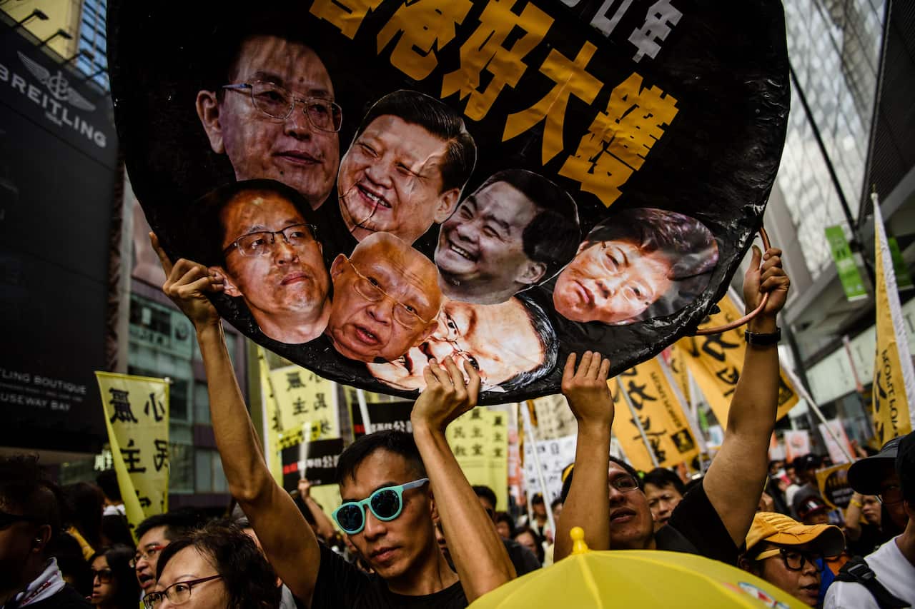 A protester holds a wok-shaped artwork with pictures showing the faces of high profile Chinese political figures including Zhang Xiaoming.