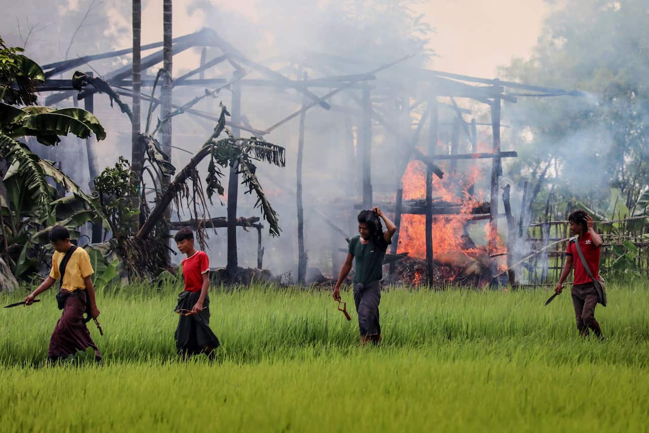 Unidentified men carry knives and slingshots as they walk past a burning house in Gawdu Tharya village near Maungdaw in Rakhine state in northern Myanmar. 