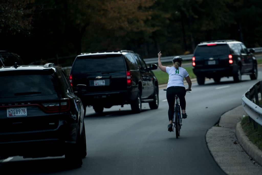 TOPSHOT - A woman on a bike gestures with her middle finger as a motorcade with US President Donald Trump departs Trump National Golf Course October 28, 2017 in Sterling, Virginia.