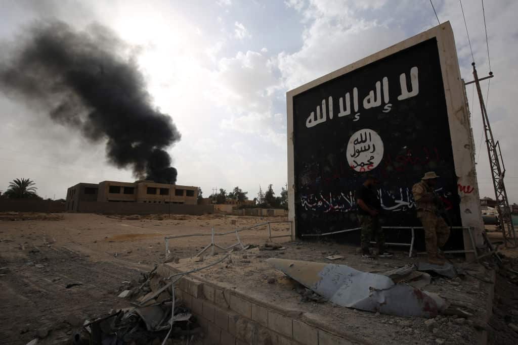 Fighters stand next to a wall bearing the IS group flag as they enter the city of al-Qaim, in Iraq's west