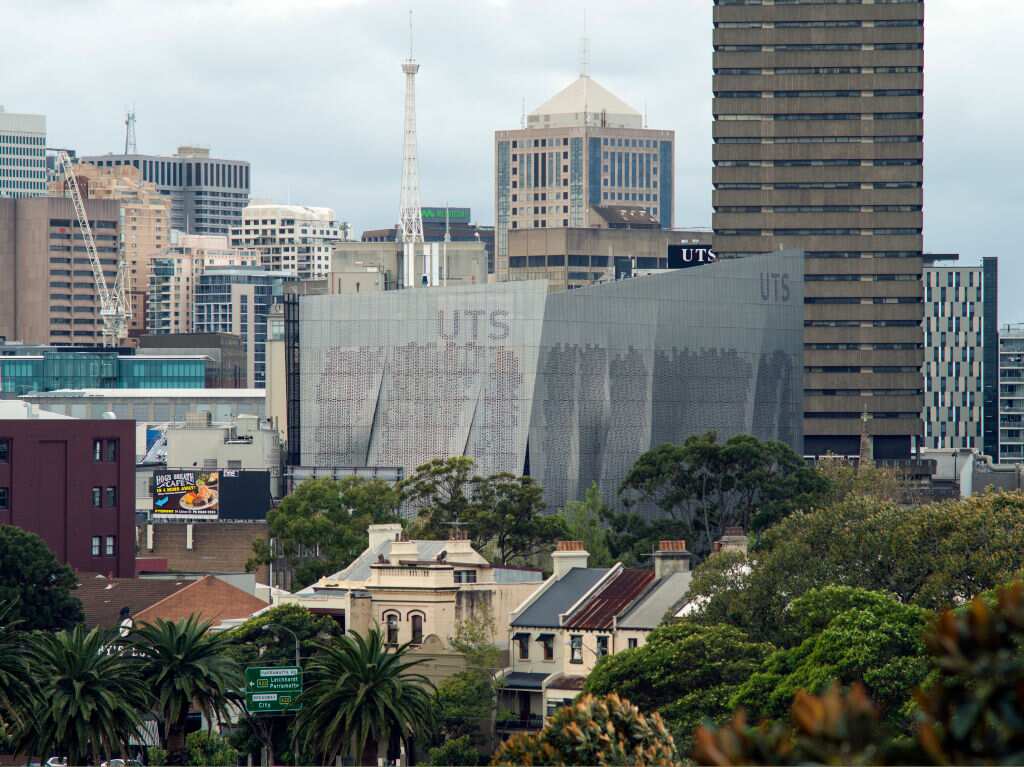 View of building above trees with city behind. Faculty of Engineering + Information Technology, University of Technology Sydney, Sydney, Australia. Architect: Denton Corker Marshall LLP, 2014.