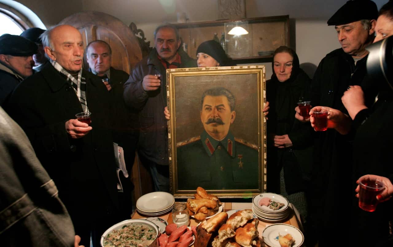 File: People toast, standing around a portrait of Soviet dictator Josef Stalin, after a memorial service at Stalin's hometown of Gori 