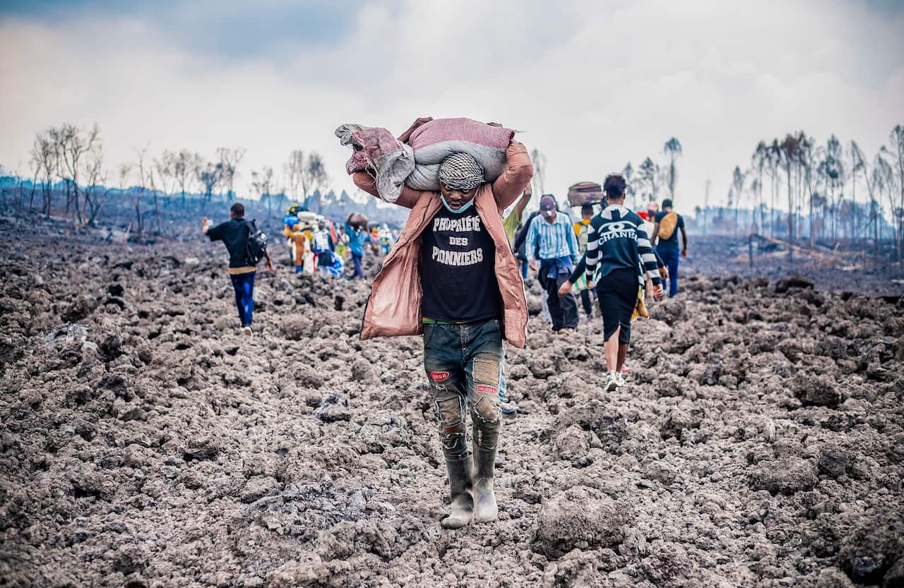 A Congolese porter helps people evacuate across cooled lava from the town of Goma in the aftermath of Mount Nyiragongo's eruption. 
