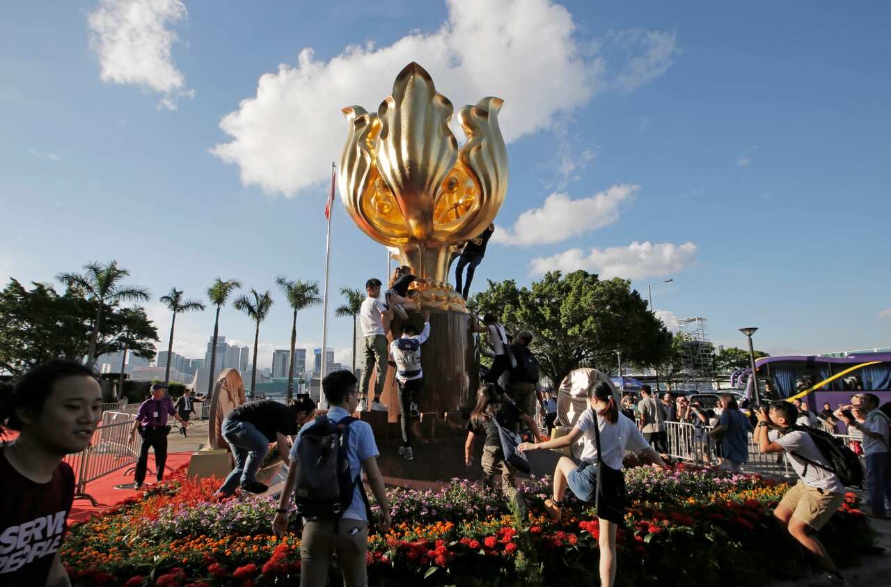 Members of the Demosisto political party and other pro-democracy activists climb up to a giant flower statue bequeathed by Beijing in 1997 (AAP)