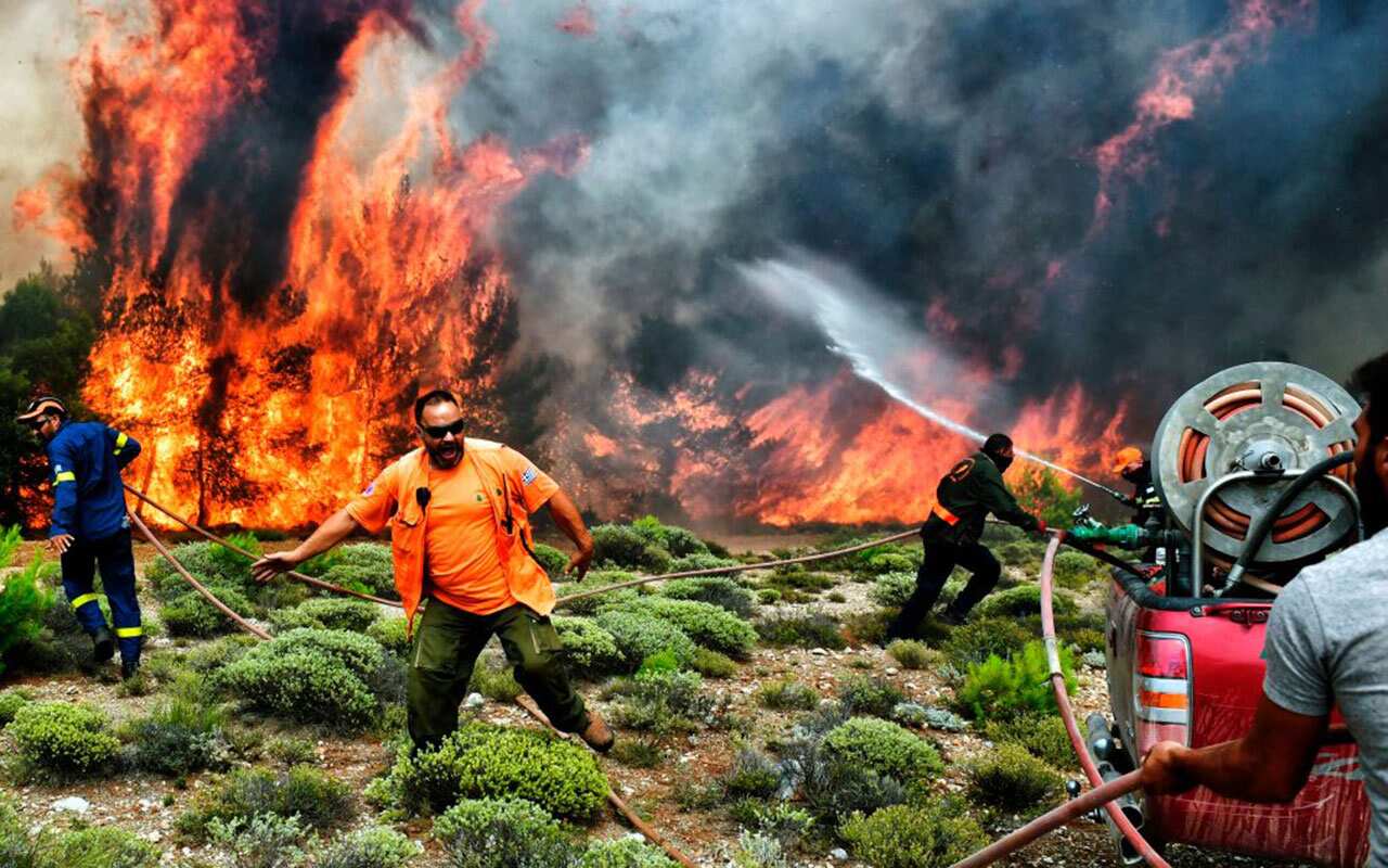 Firefighters and volunteers try to extinguish flames during a wildfire at the village of Kineta, near Athens, on July 24, 2018