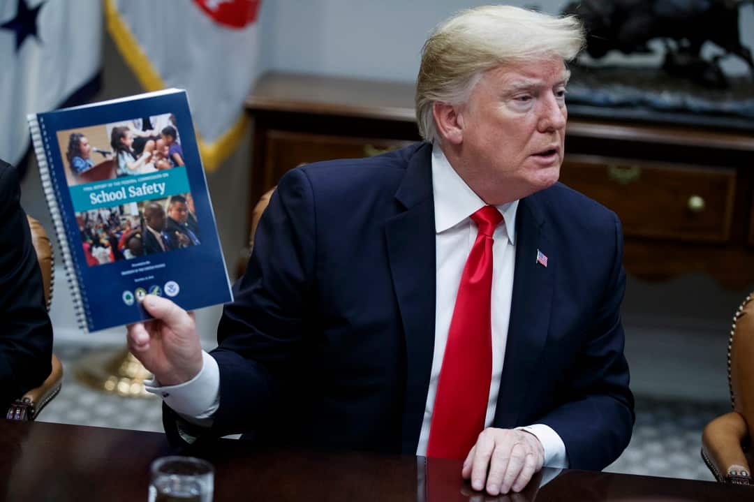 Donald Trump holds a copy of the 'Final Report of the Federal Commission on School Safety' which recommends arming some staff and using veterans as security. 