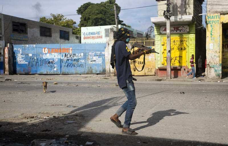 An armed civilian carries a weapon on during a shootout between rival gangs.