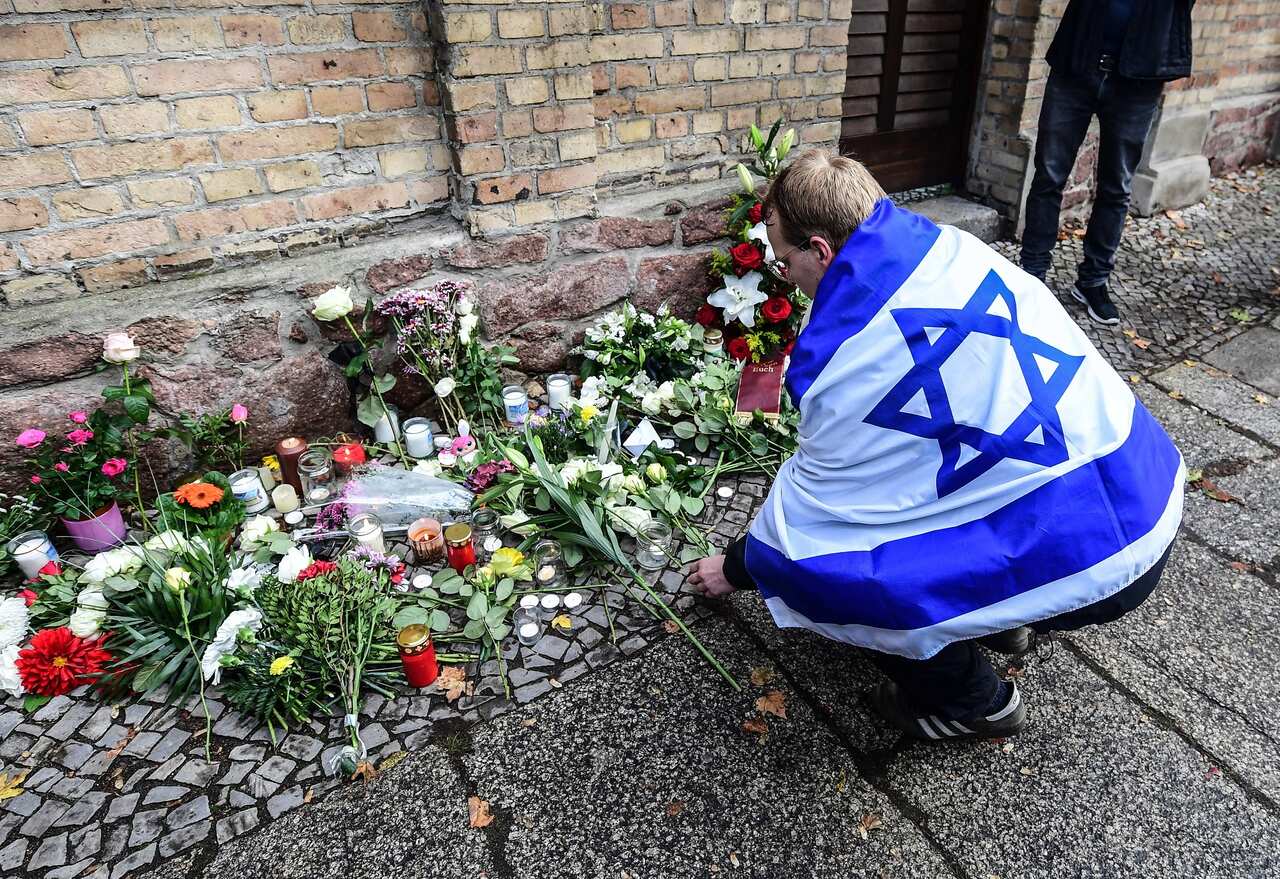 A man draped in an Israel flag lays flowers in front of the Halle synagogue that was the subject to a terrorist attack in 2019.