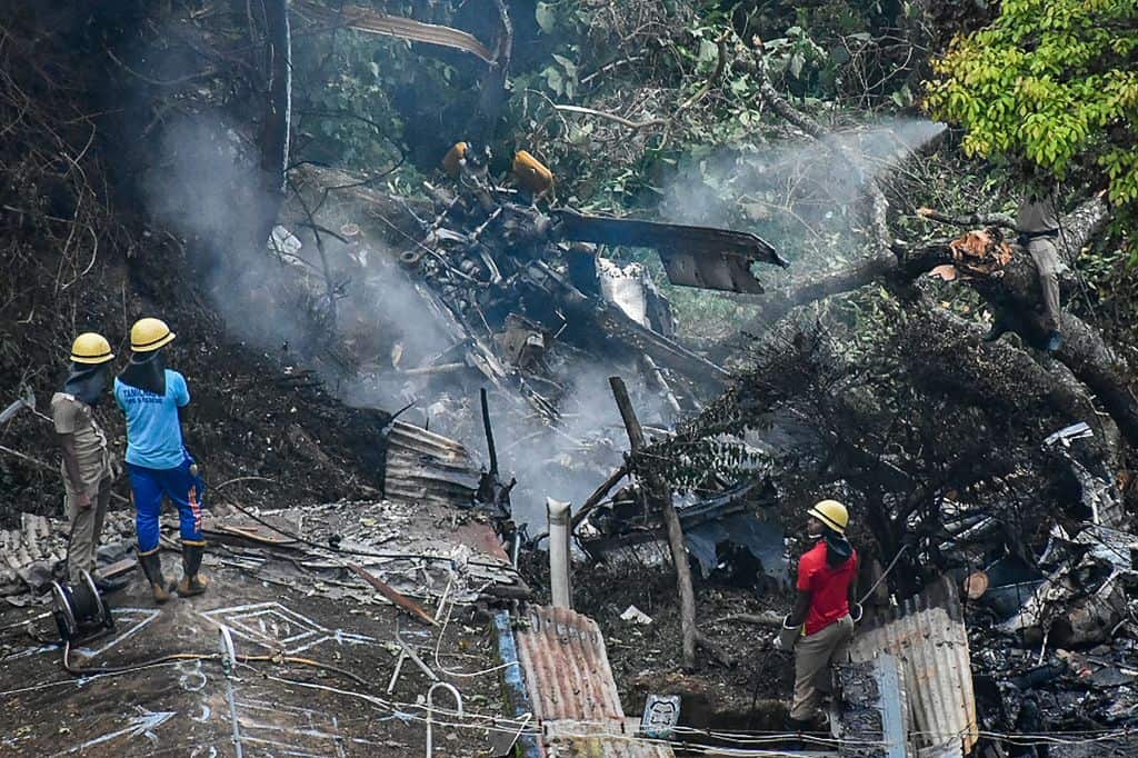Firemen and rescue workers stand next to the debris of an IAF Mi-17V5 helicopter crash site in Coonoor, Tamil Nadu, on 8 December, 2021. 