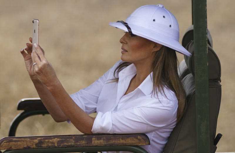 First lady Melania Trump takes photos with her cell phone during a safari at Nairobi National Park. However, her choice of headgear has been questioned.