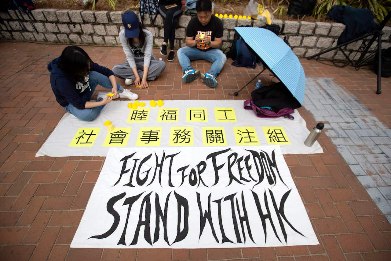 People sit near a sign reading "Fight for freedom, Stand with HK" as they fold miniature paper hard hats during a rally in Hong Kong.