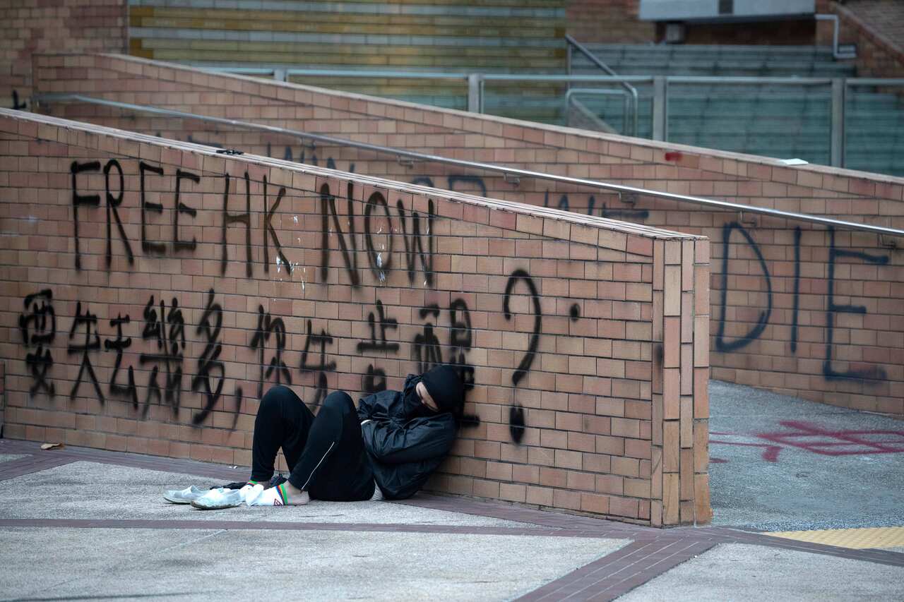 A protester sleeps in the open near graffiti which reads "How much will you lose, before you wake up" in the Hong Kong Polytechnic University.