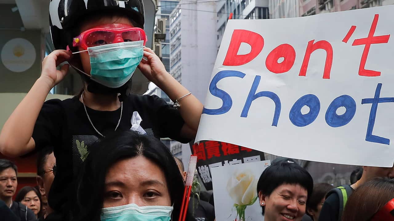 A woman and a child wearing protective gear joins tens of thousands of protesters marching through the streets in protest of an extradition bill.